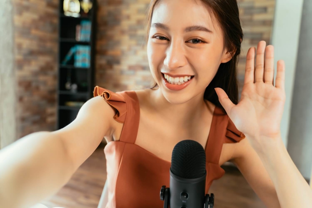 Junge Frau winkt bei einem Video Podcast in Richtung der Kamera.