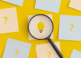 Glühbirne-Post-it unter Lupe zwischen Fragezeichen-Post-its