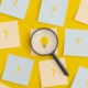 Glühbirne-Post-it unter Lupe zwischen Fragezeichen-Post-its