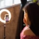 Eine Frau sitzt vor einem Smartphone und einem Ringlicht und erstellt ein Instagram Video.