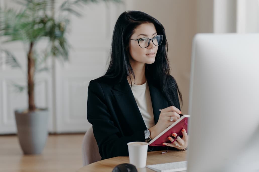 Eine neue Mitarbeiterin schaut sich ein Onboarding Video zur Wissensvermittlung an und macht sich Notizen.