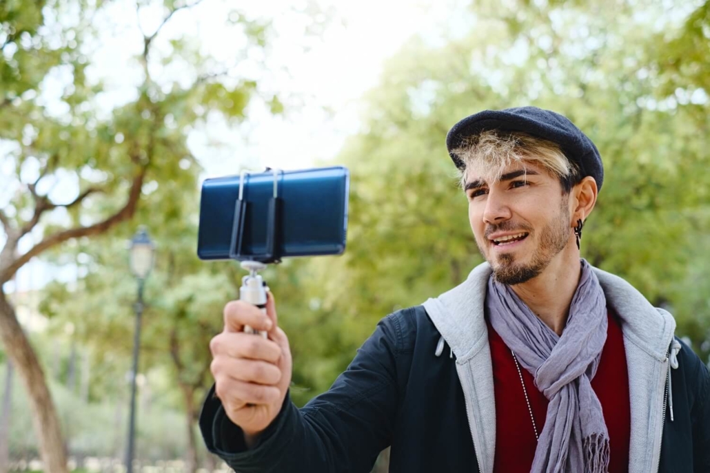 Junger Mann mit Mütze und Smartphone beim Aufnehmen eines Vlogs für den YouTube-Kanal seines Unternehmens.