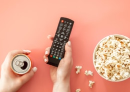 Frau hält eine Fernbedienung und Dose, um einen lustigen Werbespot zu schauen.